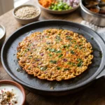 Golden brown 10-Minute Oats Vegetable Chilla on a pan with crispy edges and colorful vegetables, served with green chutney and curd.